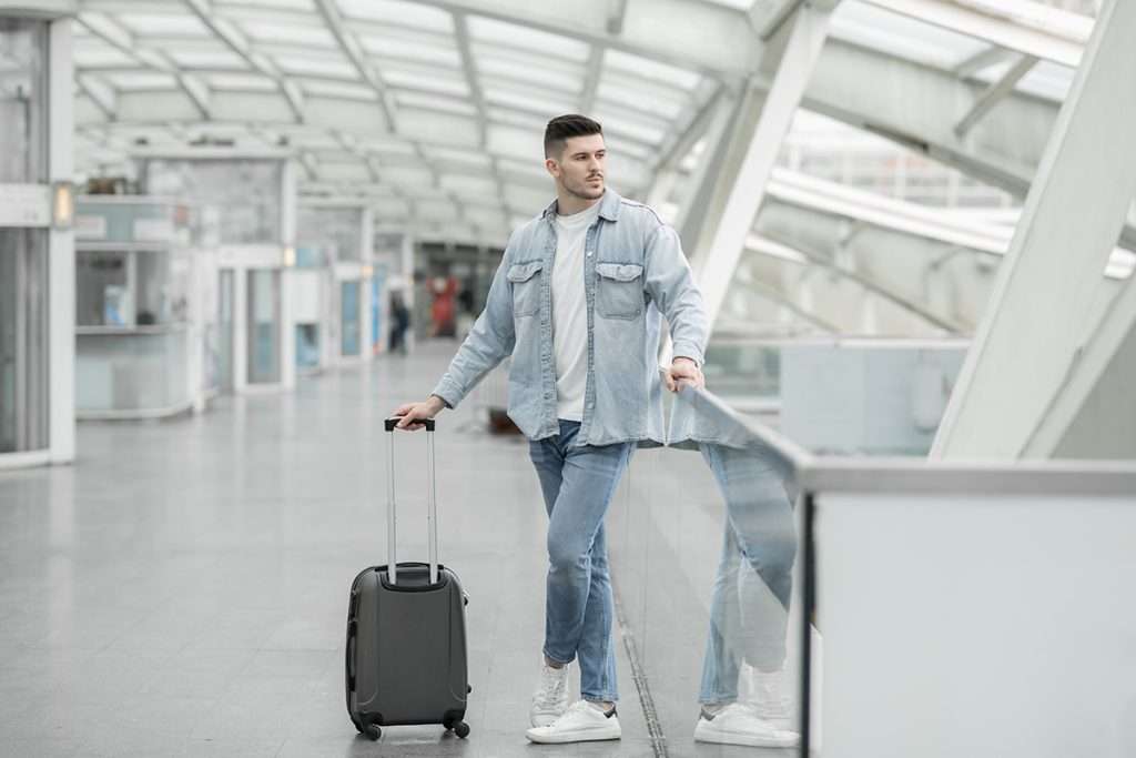 A male passenger with a suitcase waiting to travel with direct flights from Harlingen